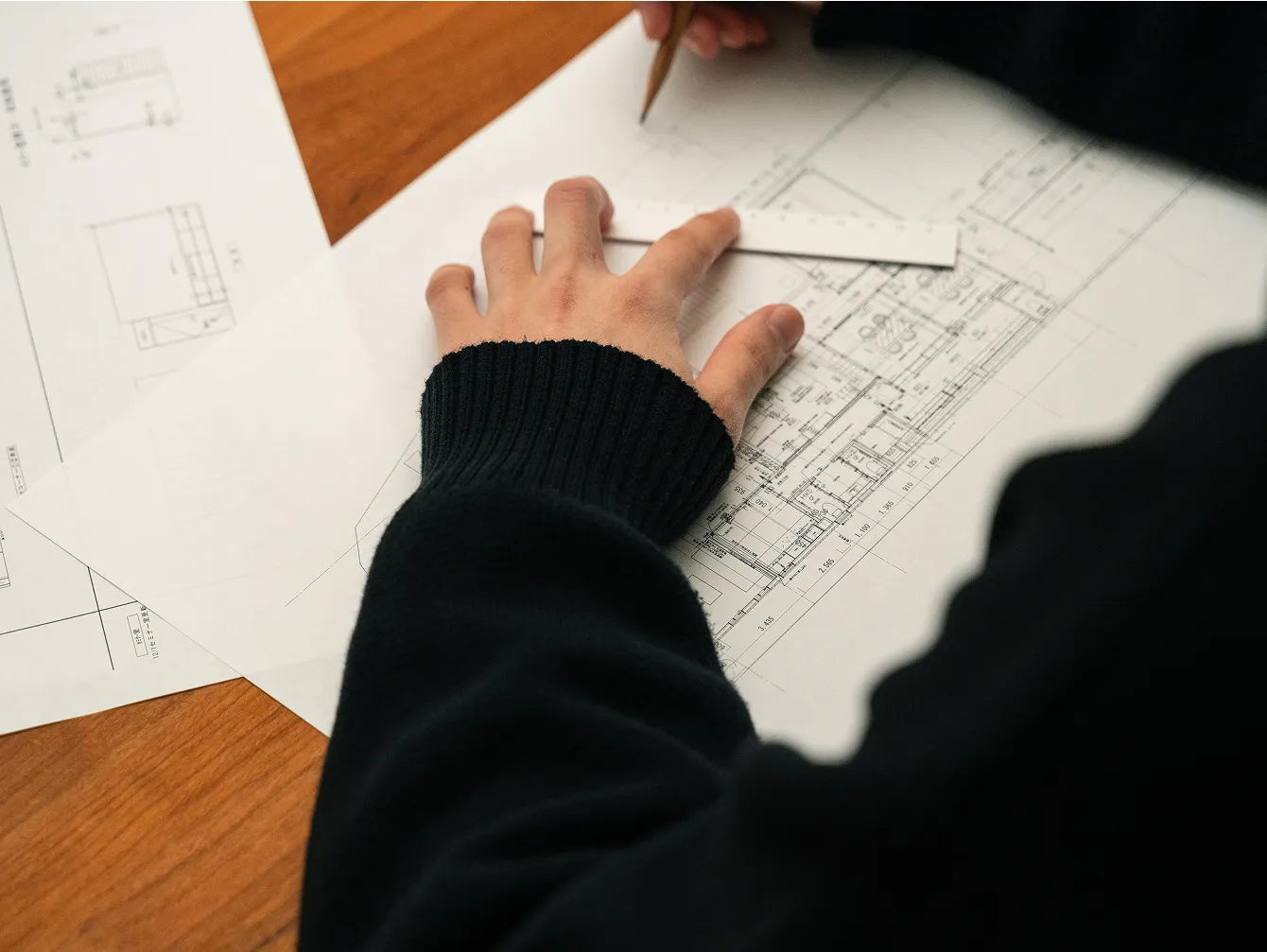 建築図面に定規を当てながら設計作業を進める人の手元